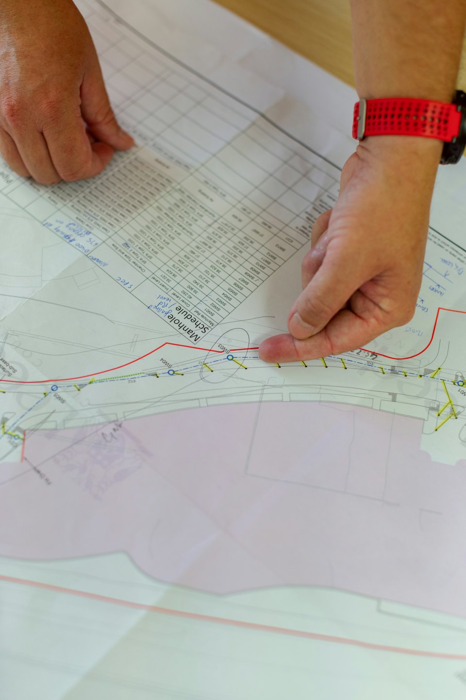 Hands pointing to a manhole schedule on a technical drawing.