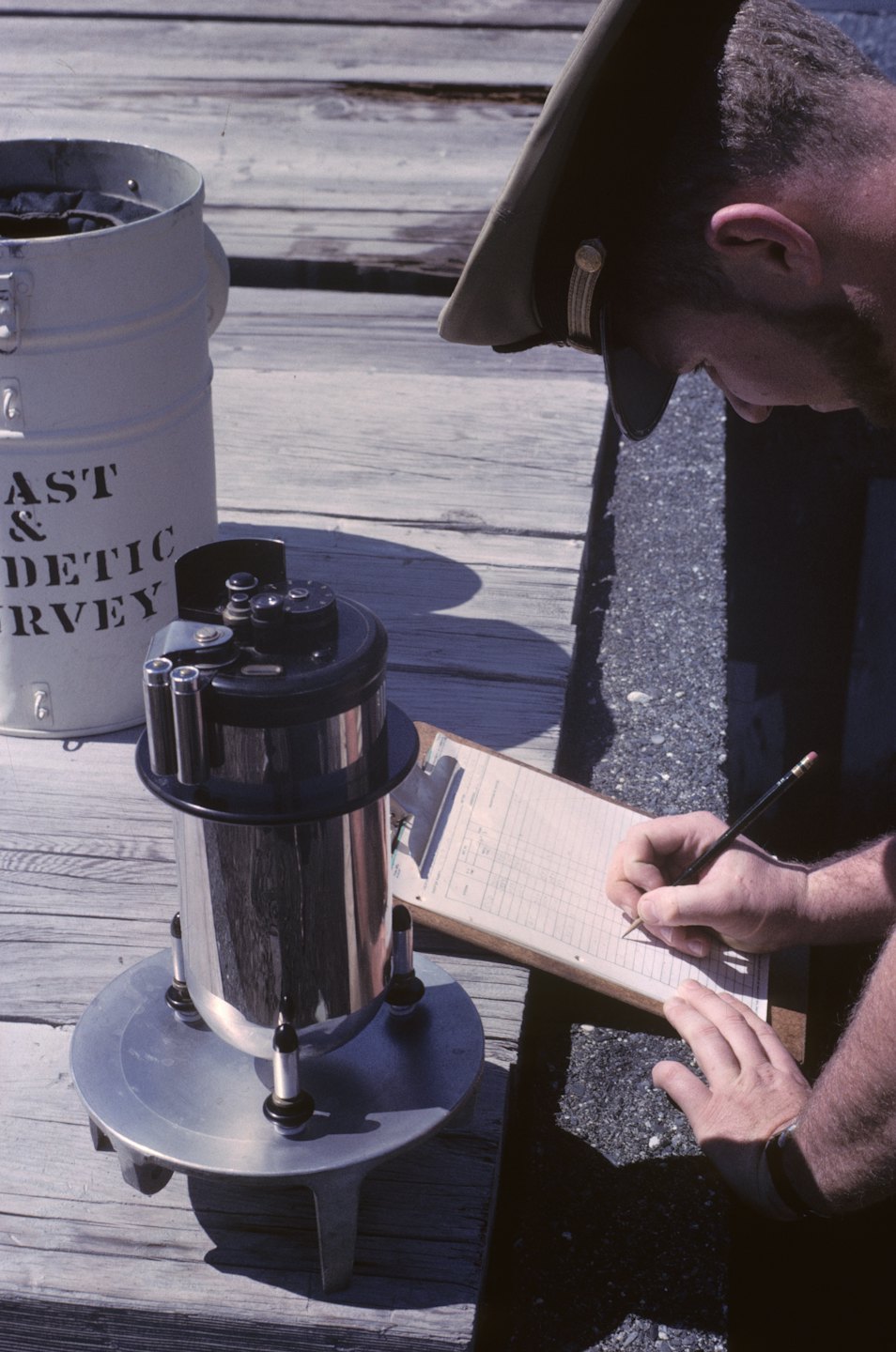 Surveyor records data on a clipboard beside a scientific instrument.